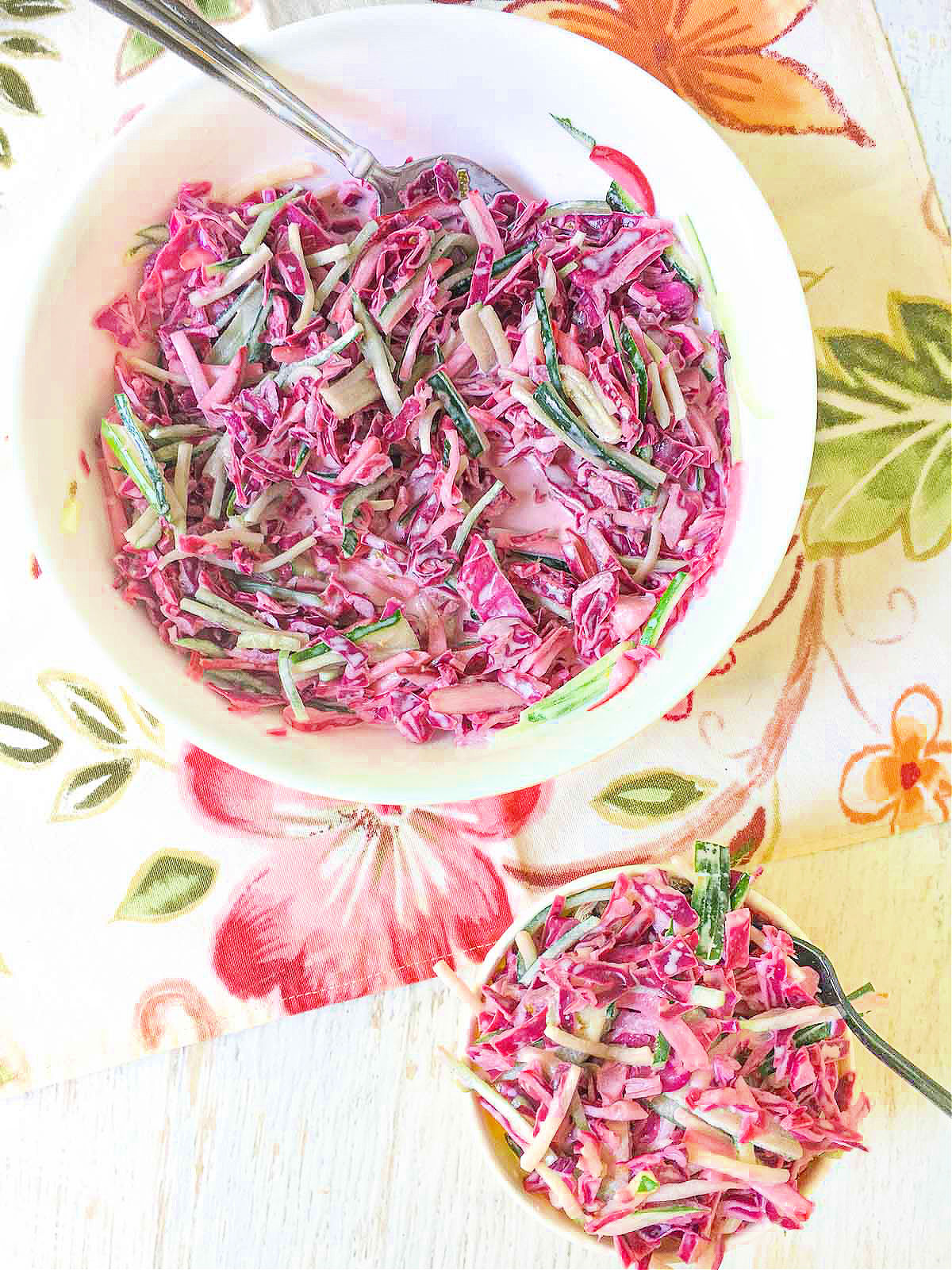 aerial view of purple cabbage salad with cucumbers in white bowl and plate