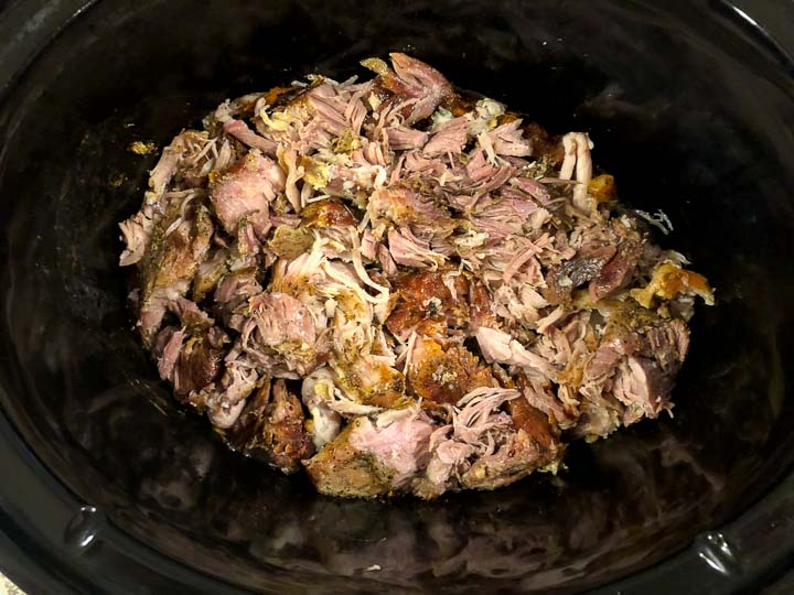 shredded garlic pulled pork in a black slow cooker crock