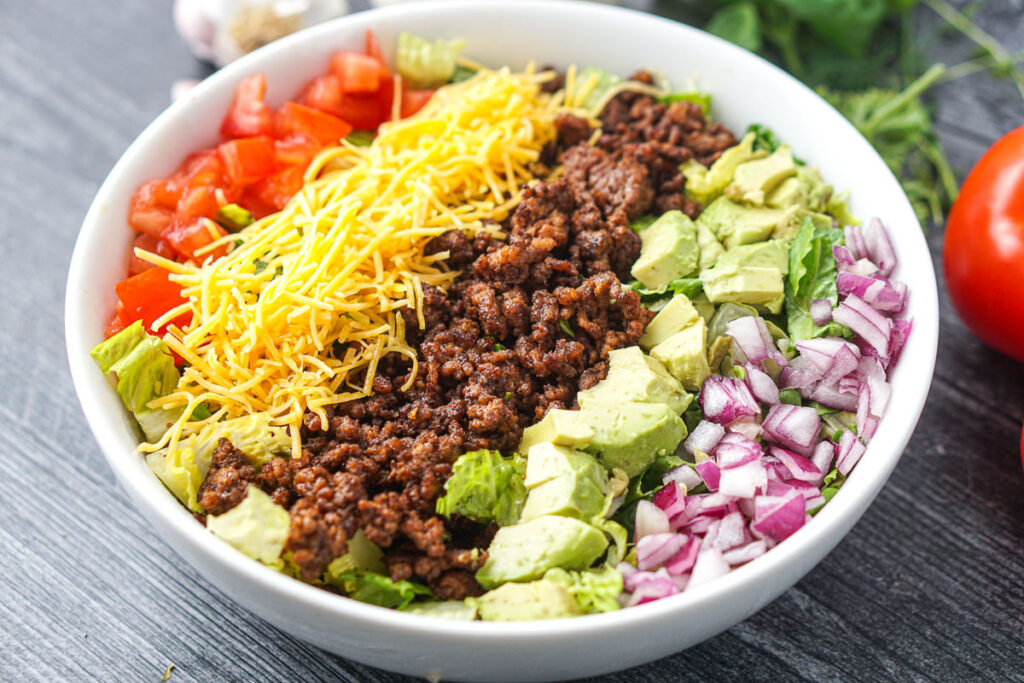 white bowl with taco salad with toppings lined up like a Cobb salad
