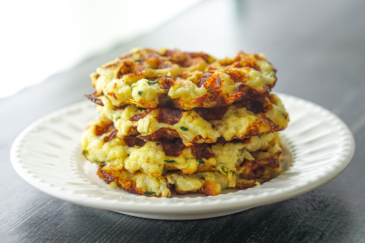 closeup of a stack of 4 keto zucchini waffles on a white plate