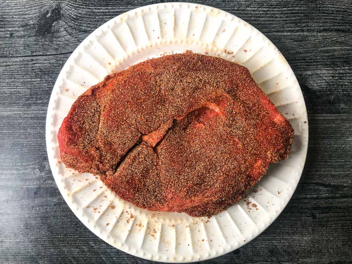 white plate with a raw chuck roast rubbed with spices
