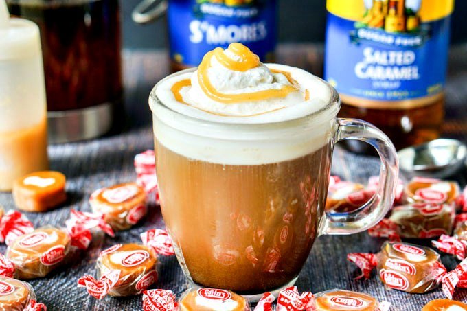 closeup of keto latte coffee with scatter caramel cream candies and Torani bottles in background