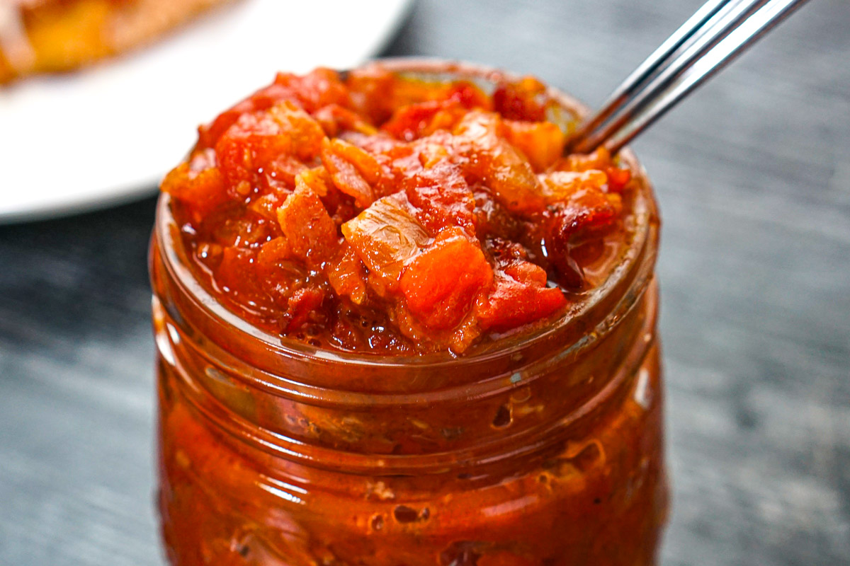 Closeup of a jar of the finished tomato bacon jam with a spoon.
