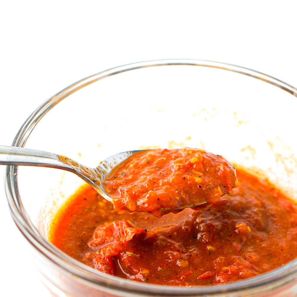 closeup of a glass bowl with homemade roasted tomato pasta sauce and a spoon