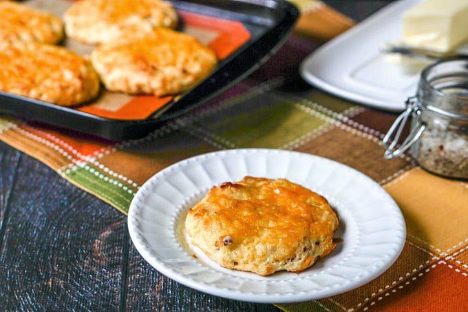  low carb bacon cheddar scones on cookie tray in background and one on white plate in foreground