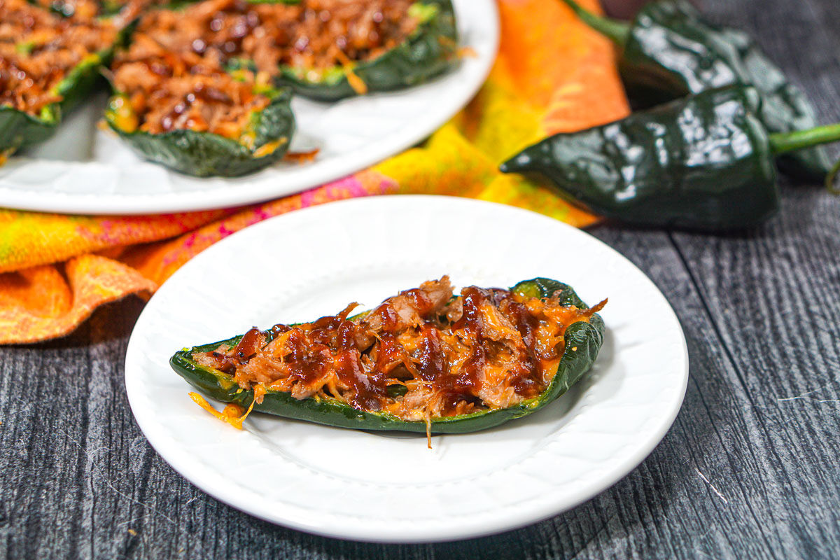 closeup of a low carb bbq pulled pork stuffed poblano pepper with a plateful in the background.