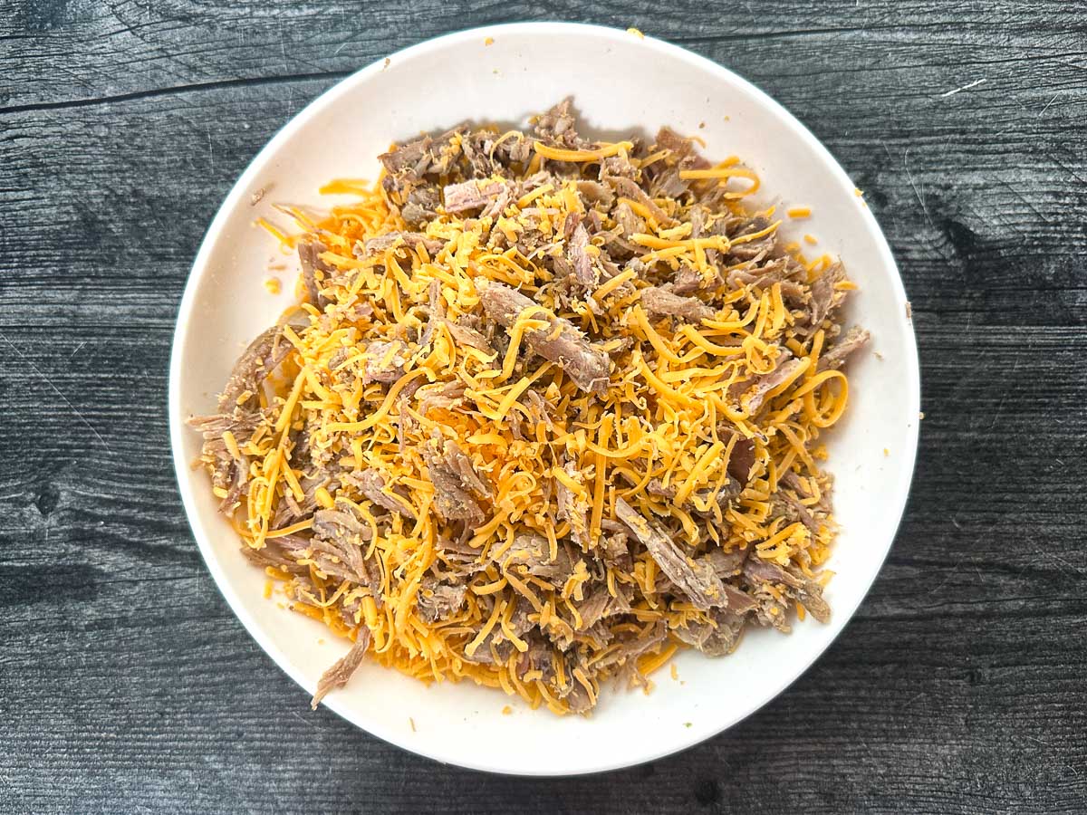 White bowl with pulled pork and cheese mixed together.