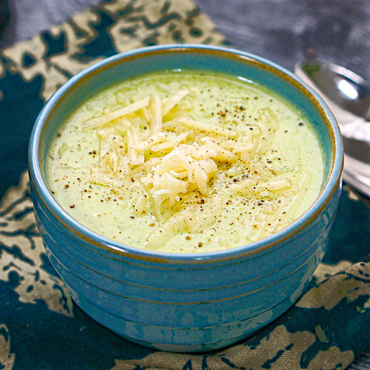 A blue bowl with a serving of creamy low carb broccoli cauliflower soup that you can make in the instant pot or stove top.