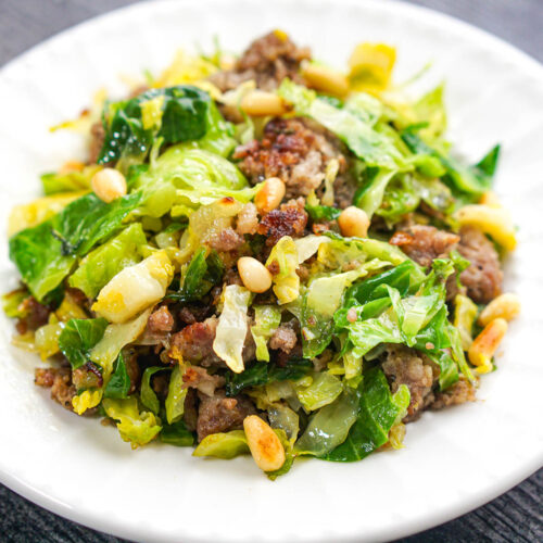 closeup of white plate with a serving of Brussel sprout hash with sausage and pine nuts