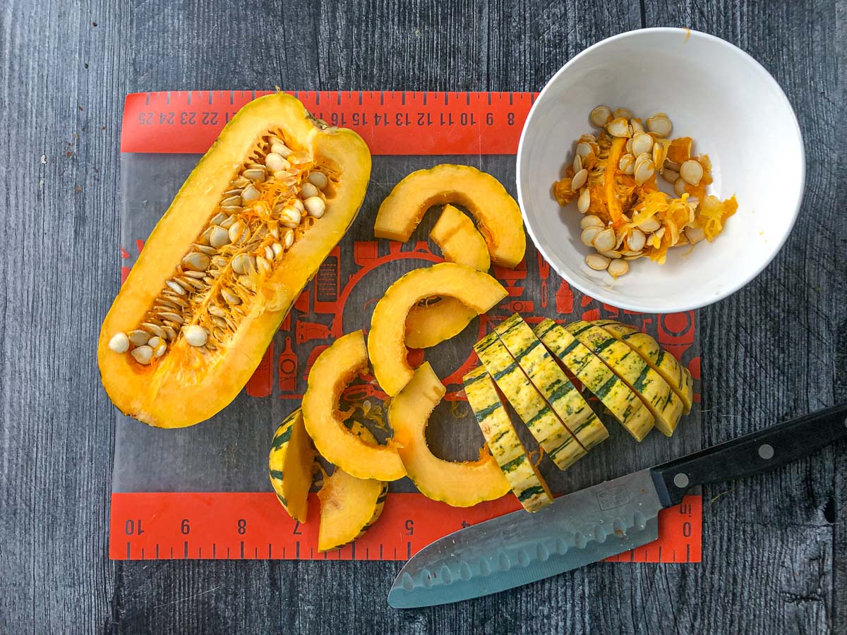 cutting board with a half of Delicata Squash and a knife and some squash rings and seeds