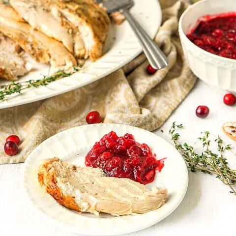 white plate with a slice of instant pot cookies turkey breast with cranberry sauce on the side