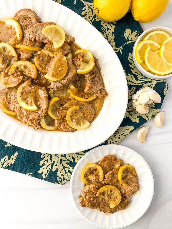 white platter and dish with lemon butter keto pork tenderloin and a bowl of sliced lemons and garlic cloves