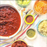 aerial view of bowls of shredded beef chili and condiments with text