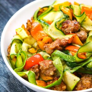 Closeup of a white bowl with the keto zucchini pasta with sausage and peppers dish.