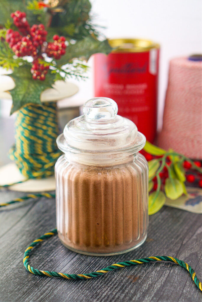 closeup of a jar of keto hot chocolate mix and green and gold rope and red and white spool of tread in the background