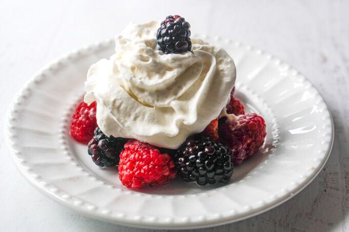 White plate with drunken berries and whipped cream.