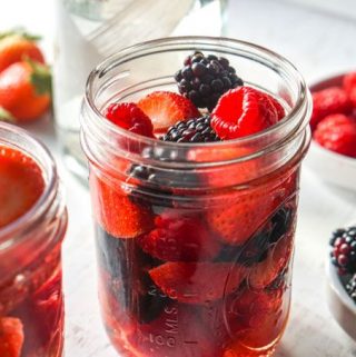 Closeup photo of a jar of strawberries and raspberries and another jar with blackberries and strawberries.