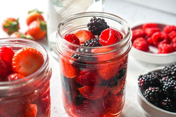 Closeup photo of a jar of strawberries and raspberries and another jar with blackberries and strawberries.