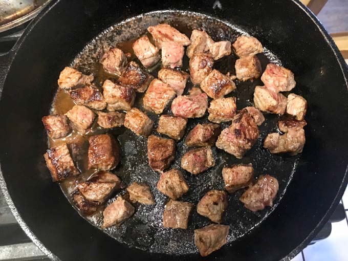 Cast iron skillet with steak bites being cooked.