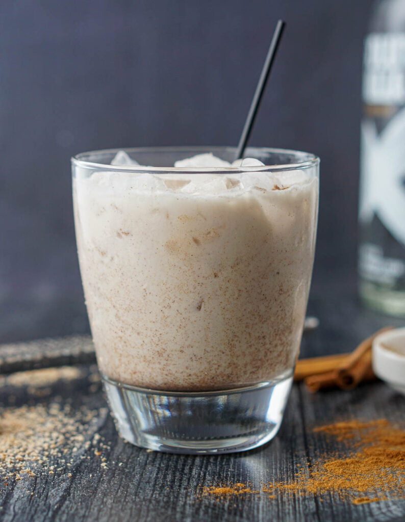 glass with low carb vodka chata drink with a vodka bottle in the background and ground cinnamon and nutmeg scattered