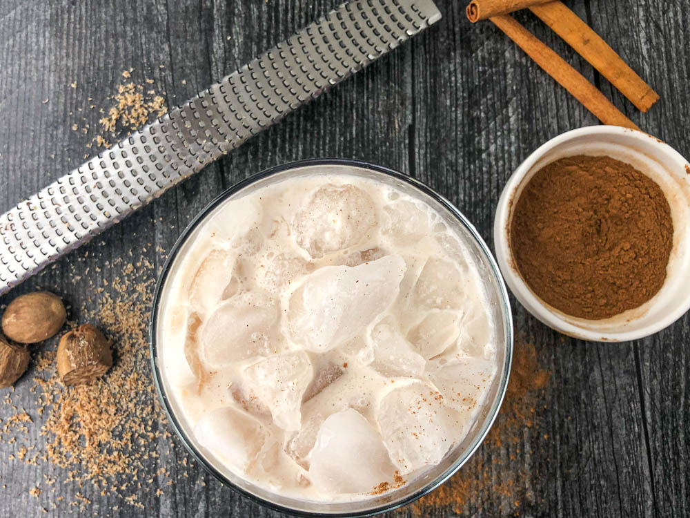 aerial view of a glass filled with crushed ice and low carb creamy horchata drink with a microplane and cinnamon sticks