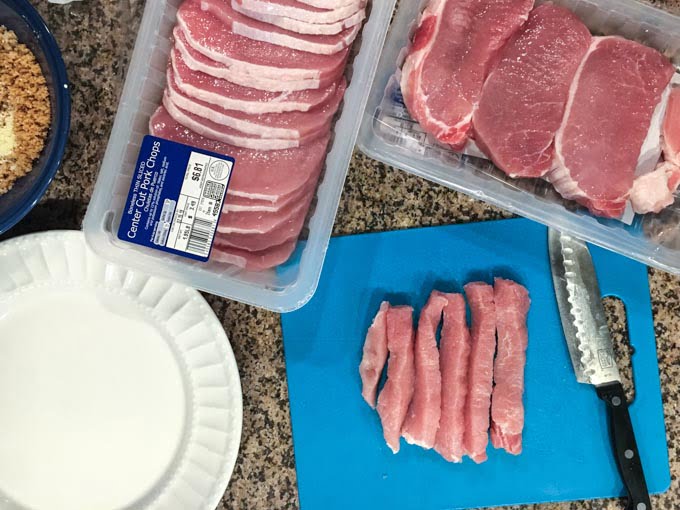 Photo of raw pork chops and a cutting board with cut up pork fries and a knife.