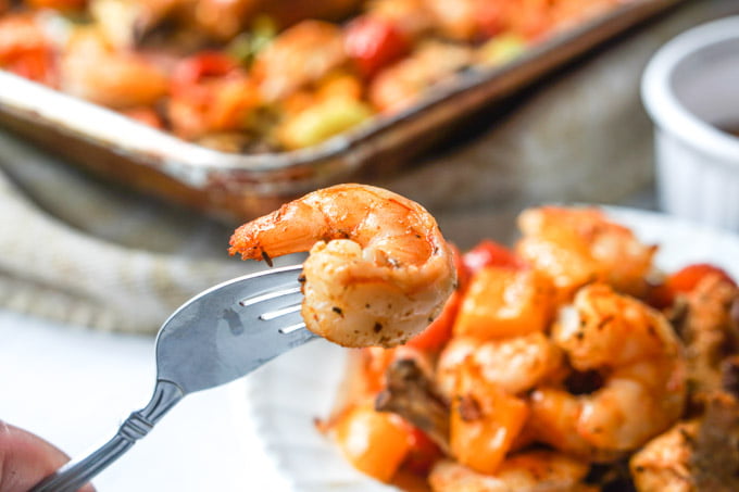 Photo of a fork with a cajun shrimp on it and a plate and sheet pan in background.