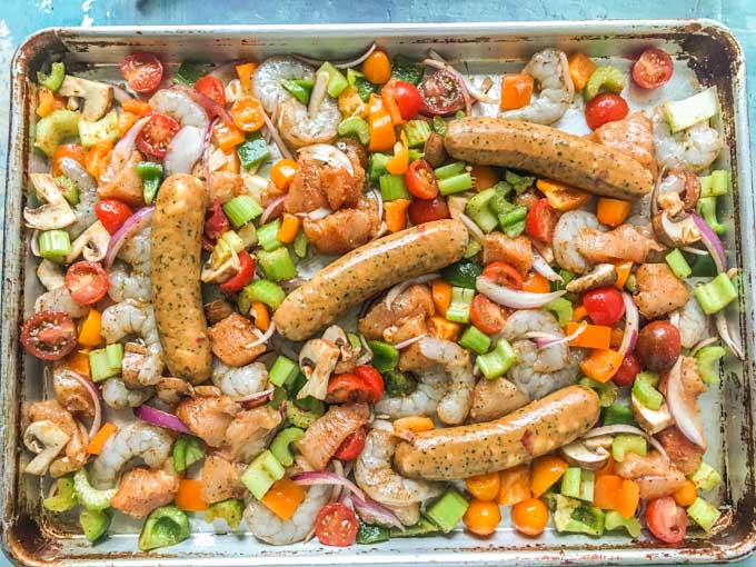 Sheet pan full of raw ingredients for this cajun chicken, shrimp, sausage and vegetables.