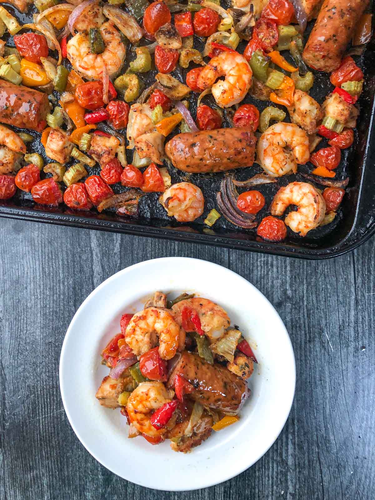 aerial view of a baking sheet and white plate with cajun shrimp, sausage, chicken and veggies