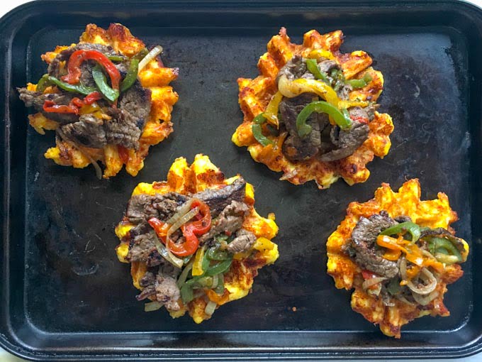 Cheese waffles on a cookie sheet topped with cheesesteak