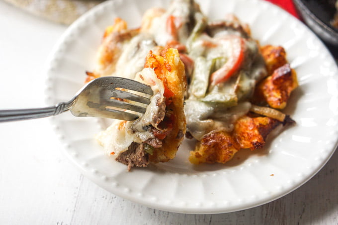 A cheese waffle with cheesesteak topping and fork with a bite on it.