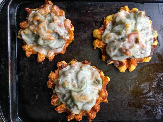 3 cheese waffles with Philly cheesesteak on top all on a cookie sheet.