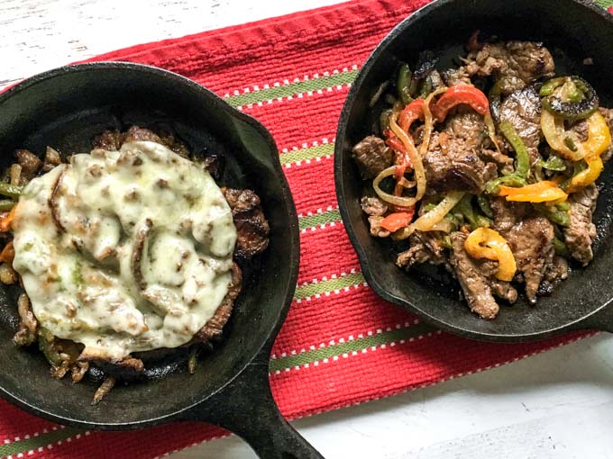 2 mini cast iron skillets with cheesesteak filling inside and red tea towel.