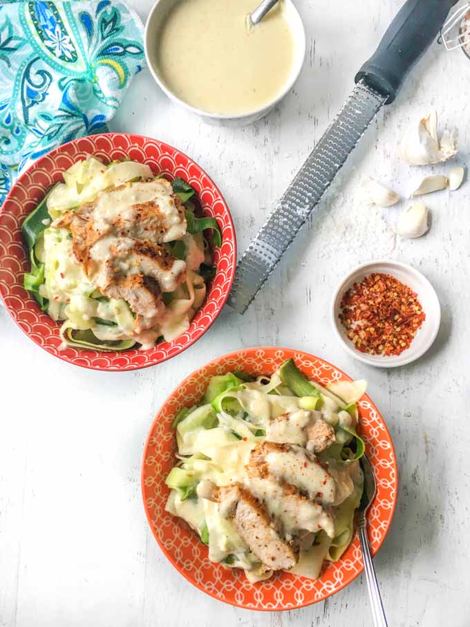Two orange bowls with zucchini noodles, chicken and keto alfredo sauce.