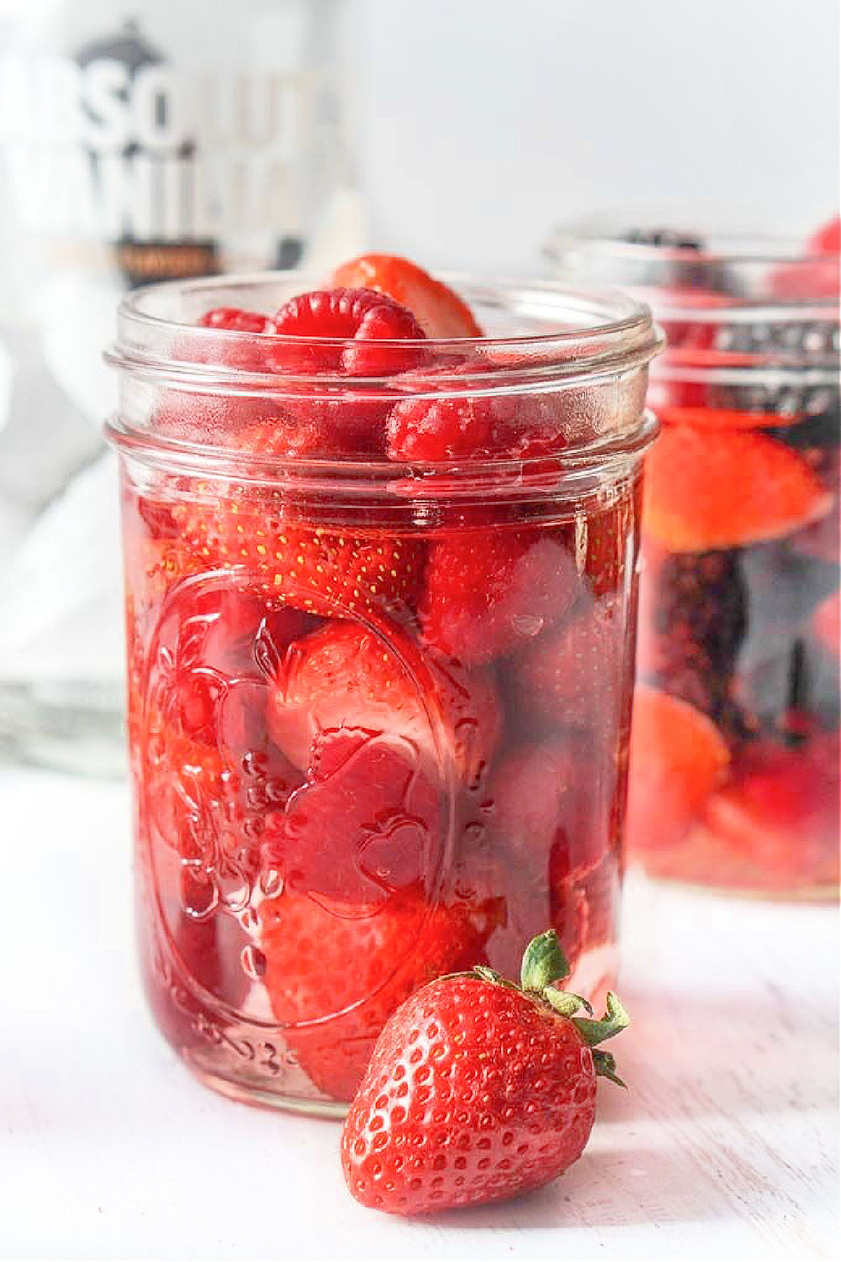 Closeup of a jar full of keto drunken berries and a bottle of Absolut vanilla vodka in the background.
