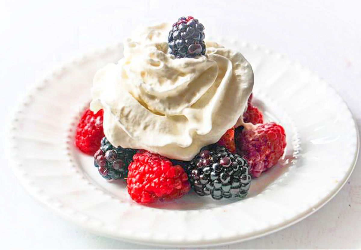 White plate with alcohol soaked berries and fresh whipped cream on top.