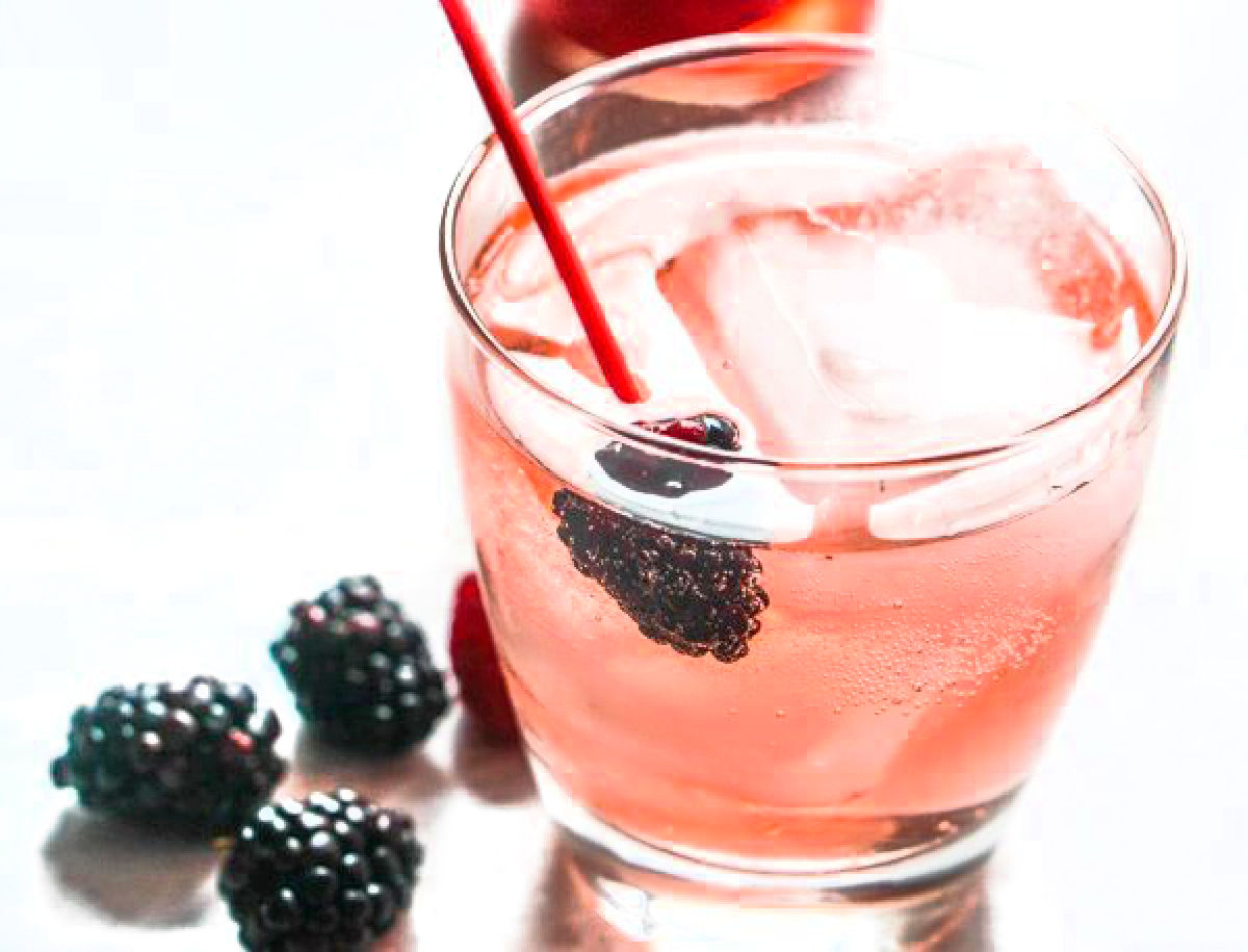 A cocktail glass with the berry soaked vodka and ice and fresh blackberries next to it.
