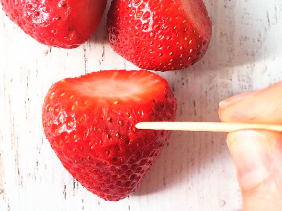 Fresh strawberry with a toothpick putting holes in it to absorb the vodka.