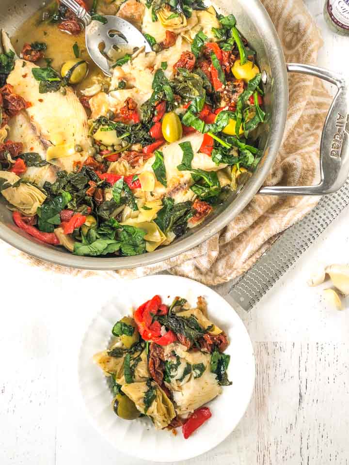 white plate and pan with Tilapia, spinach, peppers, artichokes and olives 