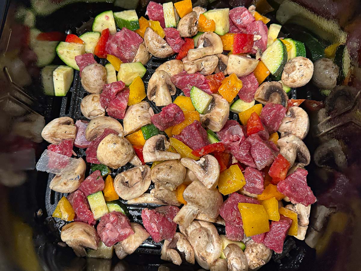 Air fryer basket with the hibachi steak and vegetables, ready to cook.