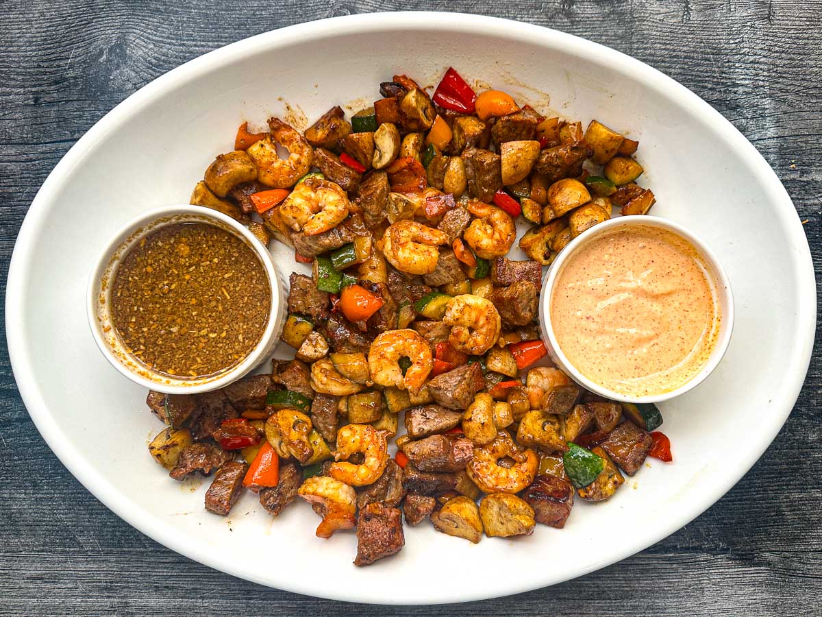 Aerial view of white platter with hibachi steak and shrimp appetizer with 3 dipping sauces.