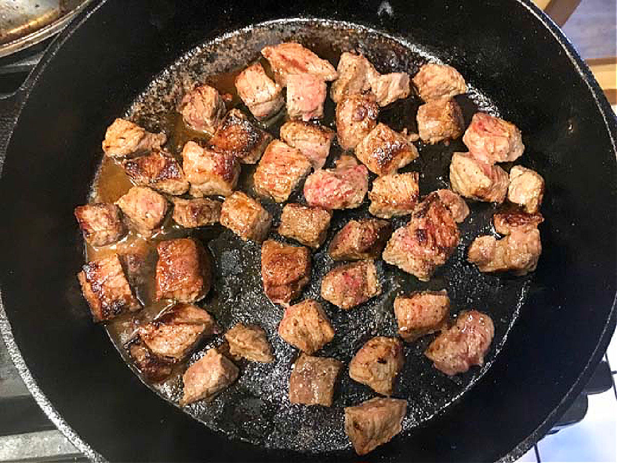 Cast iron skillet with meat bites cooking.