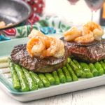 Photo of steaks on asparagus with shrimp pan in back.