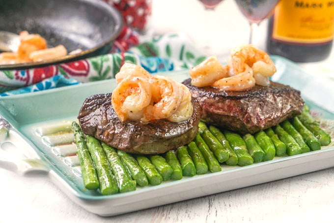 Photo of steaks on asparagus with shrimp pan in back.