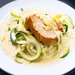 white plate with zucchini noodles in keto Alfredo sauce and a slice of chicken