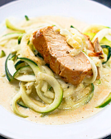 white plate with zucchini noodles in keto Alfredo sauce and a slice of chicken