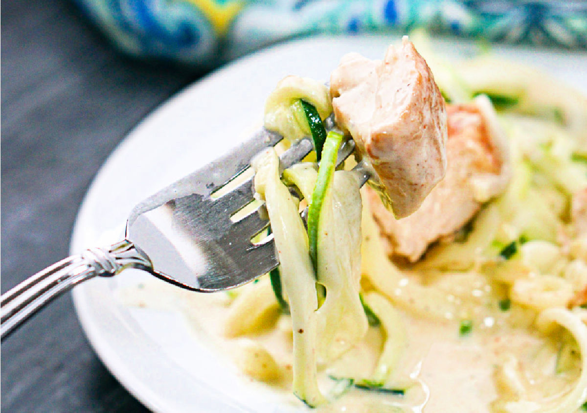 closeup of a forkful of zucchini noodles with creamy sauce and chicken