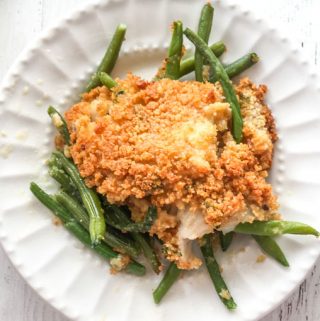 white plate with baked fish on a bed of green beans