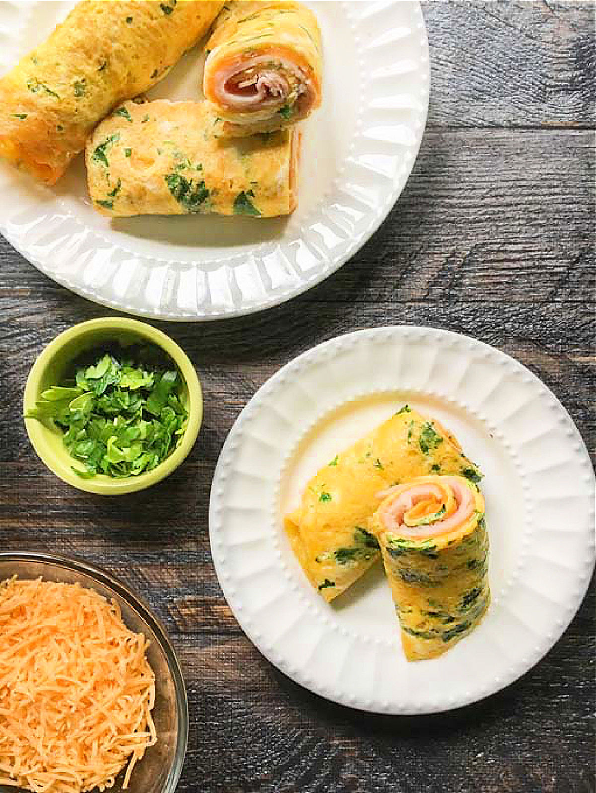 aerial view of white plates with herb keto egg wraps and fresh chopped herbs, cheese and fresh eggs