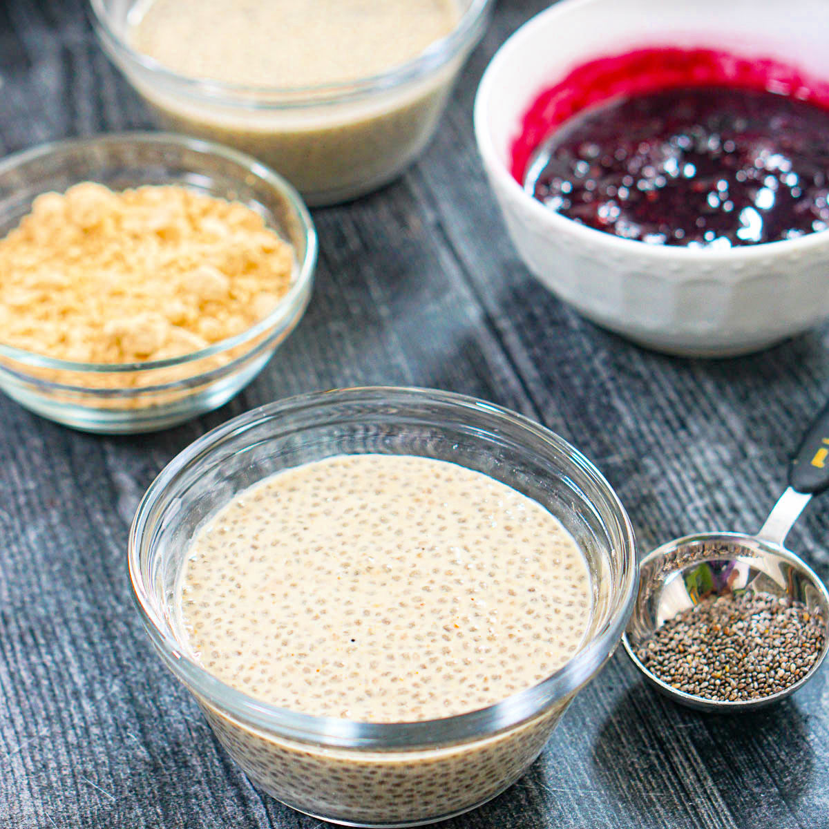 A glass bowl with the pb dessert and bowls of the berry sauce and pb powder in the background.